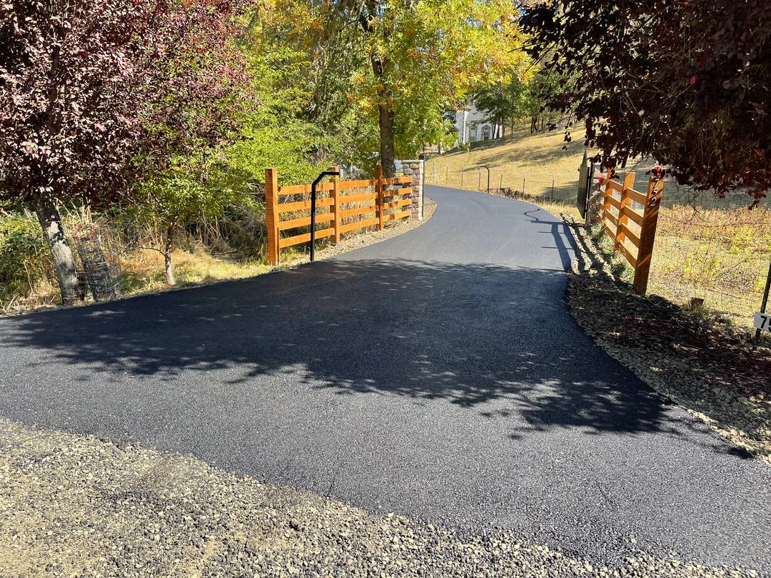 Curving asphalt driveway lined with wooden rail fencing and autumn trees